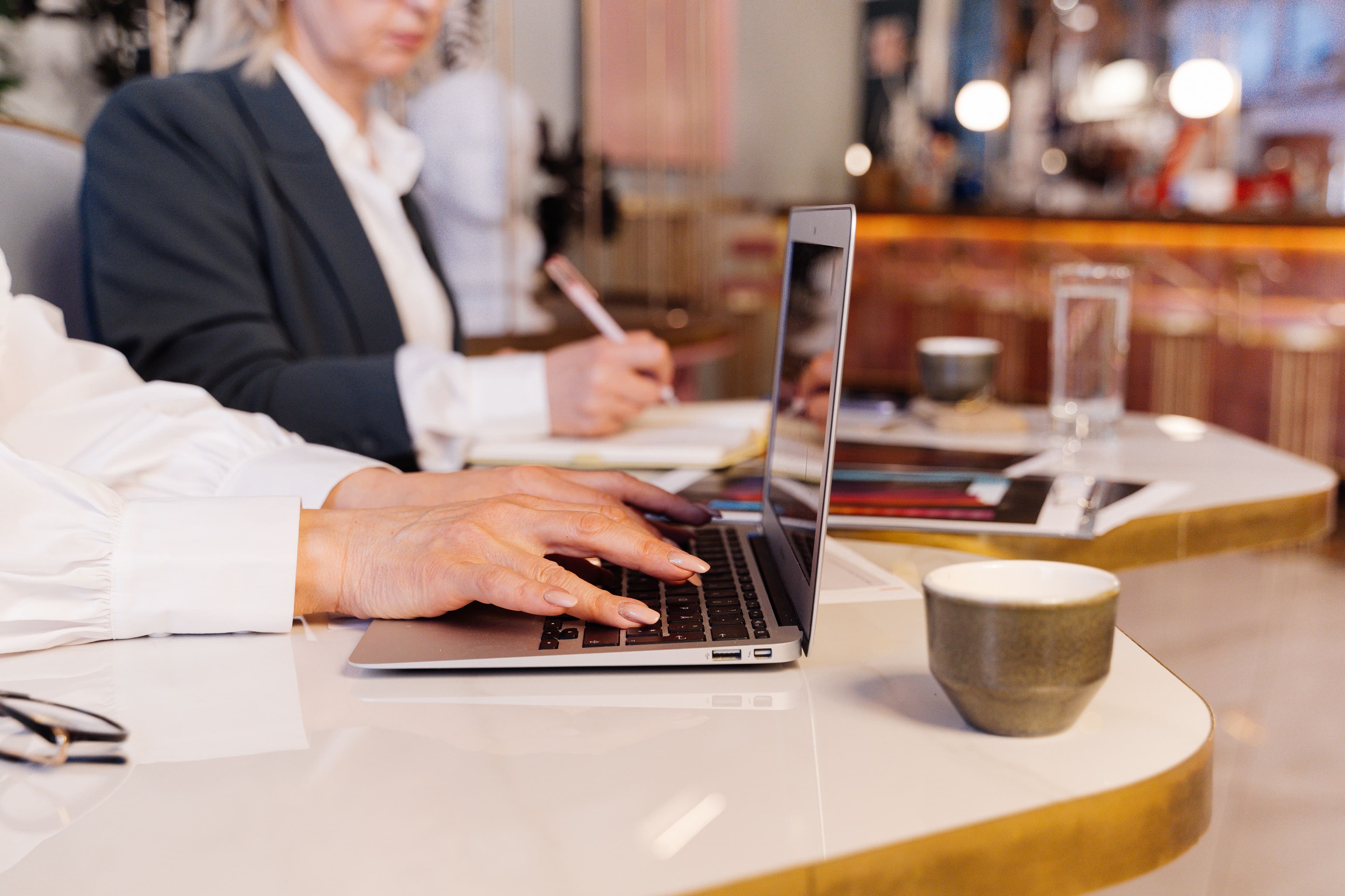 A person working on a laptop at a café table beside a cup of coffee.